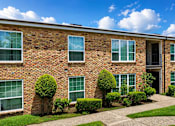 Thumbnail 5 of 10 - A brick building with green bushes in front.