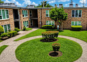 Thumbnail 6 of 10 - A courtyard with a tree and bushes in the middle of a brick building.