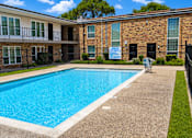 Thumbnail 4 of 10 - A swimming pool in front of a brick building with a sign that says "For Rent".