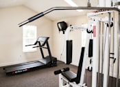 Thumbnail 9 of 23 - A home gym with a treadmill, weights, and exercise equipment.