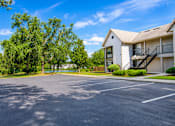 Thumbnail 24 of 26 - A large, empty parking lot in front of a two-story apartment building with a black metal staircase leading to the second floor.