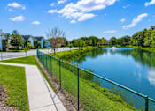Thumbnail 18 of 26 - A serene park with a lake, a fence, and a walking path.