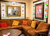 Thumbnail 4 of 6 - A living room with a brown couch, a round table, and a mirror on the wall.