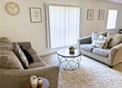 Thumbnail 7 of 17 - A living room with a grey couch, a coffee table, and a clock on the wall.