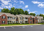 Thumbnail 1 of 19 - A row of apartment buildings with a parking lot in front.