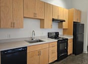 Thumbnail 12 of 16 - A kitchen with black appliances and wooden cabinets.at South Main Artspace Lofts, Memphis, TN 38126