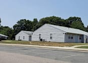 Thumbnail 2 of 4 - A white building with a grey roof is surrounded by a parking lot.