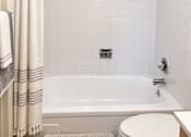 Thumbnail 32 of 33 - A white tiled bathroom with a white bathtub and toilet.