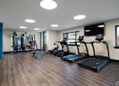 Thumbnail 25 of 28 - A gym with treadmills, weights, and a television.