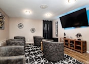 Thumbnail 24 of 28 - A living room with a large grey chair in the center and a flat screen TV mounted on the wall.