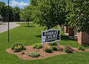 Thumbnail 2 of 3 - A sign for Forest Court Apartment Homes is in the foreground of a grassy area.