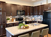 Thumbnail 36 of 43 - A kitchen with brown cabinets and a black refrigerator.