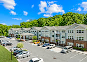 Thumbnail 3 of 10 - A parking lot in front of a large building with cars parked.