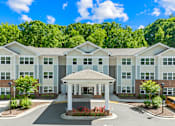Thumbnail 1 of 10 - A building with a white and grey facade surrounded by greenery.