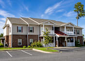 Thumbnail 1 of 12 - A large two-story apartment building with a parking lot in front.