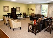 Thumbnail 4 of 7 - A living room with a black couch, a coffee table, and a dining table with chairs.