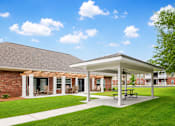 Thumbnail 6 of 12 - A covered patio area with a picnic table in front of a brick building.