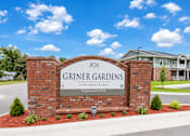 Thumbnail 2 of 12 - A sign for Griner Gardens Apartment Homes stands in front of a house.