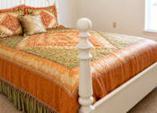 Thumbnail 19 of 19 - A bed with a white headboard and orange bedspread with a green and orange pillow.