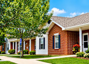Thumbnail 15 of 19 - A red brick house with a white porch and a tree in front.