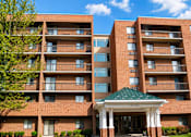 Thumbnail 3 of 3 - A large brick building with a green roof and a covered walkway entrance.
