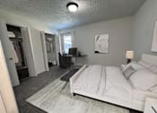 Thumbnail 8 of 18 - A bedroom with a bed, desk, and clothing rack.