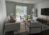 Thumbnail 1 of 18 - A living room with a grey couch, a white armchair, a coffee table, and a television.