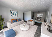 Thumbnail 13 of 18 - A living room with a white couch, a blue ottoman, and a white coffee table.