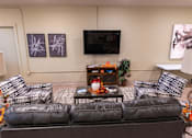 Thumbnail 9 of 17 - A living room with a black leather couch and a coffee table with a vase of flowers on it.