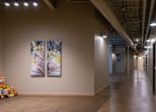 Thumbnail 14 of 17 - A long hallway with two paintings on the wall and a teddy bear on the floor.