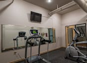Thumbnail 4 of 25 - A gym with treadmills, a stationary bike, and a television mounted on the wall.