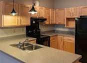 Thumbnail 24 of 25 - A kitchen with wooden cabinets and black appliances.