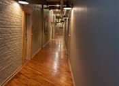 Thumbnail 5 of 25 - A long hallway with wooden floors and brick walls.