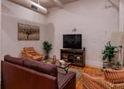 Thumbnail 10 of 25 - A living room with a brown leather couch and a television.