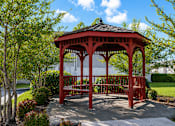 Thumbnail 3 of 7 - A red gazebo is surrounded by trees and bushes.