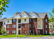 Thumbnail 6 of 20 - A large red brick apartment building with a white trim and a black roof.
