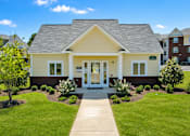 Thumbnail 7 of 20 - A small yellow house with a grey roof and a white door.