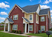 Thumbnail 1 of 17 - A red brick house with a white roof and a green lawn in front.