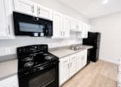 Thumbnail 6 of 9 - A black stove and microwave in a kitchen with white cabinets.