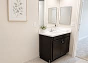 Thumbnail 6 of 12 - A bathroom with a black vanity and a framed leaf picture on the wall.