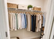 Thumbnail 12 of 12 - A white closet with clothes hanging and a basket on the floor.