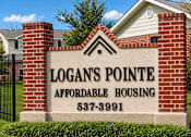 Thumbnail 4 of 14 - A sign for Logan's Pointe Affordable Housing stands in front of a house.
