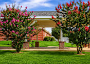 Thumbnail 3 of 14 - A building with a covered walkway is flanked by two trees with pink flowers.
