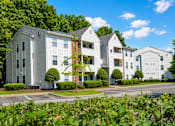 Thumbnail 18 of 18 - A white building with a red brick chimney is surrounded by greenery.