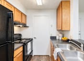 Thumbnail 22 of 37 - A kitchen with a black fridge and wooden cabinets.