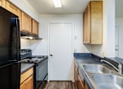 Thumbnail 5 of 20 - A kitchen with a black refrigerator, wooden cabinets, and a white door.
