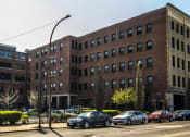 Thumbnail 24 of 34 - a large brick building on a city street with cars parked