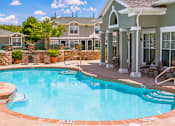 Thumbnail 2 of 9 - A pool with a stone border and a house in the background.