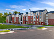 Thumbnail 1 of 15 - A large apartment complex with a parking lot in front.