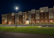 Thumbnail 8 of 15 - Apartment building at night with lights on.